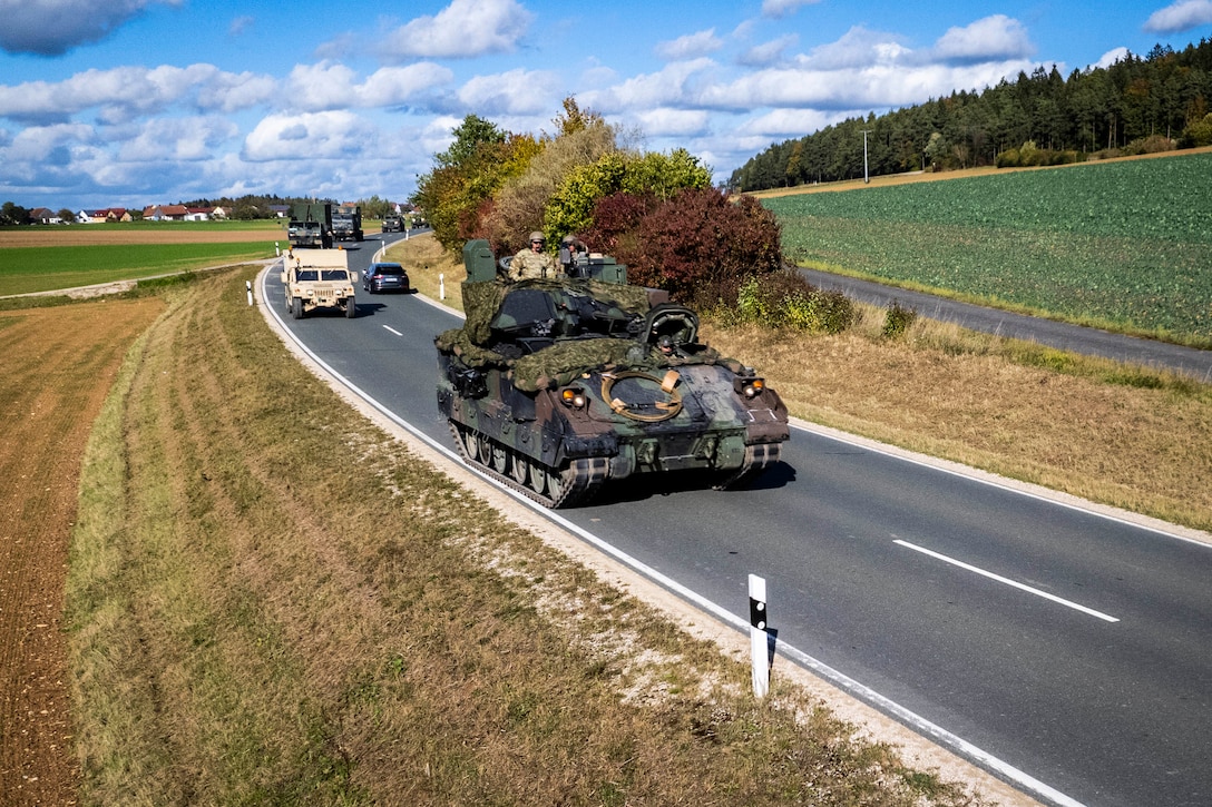 Military vehicles drive along a country road.