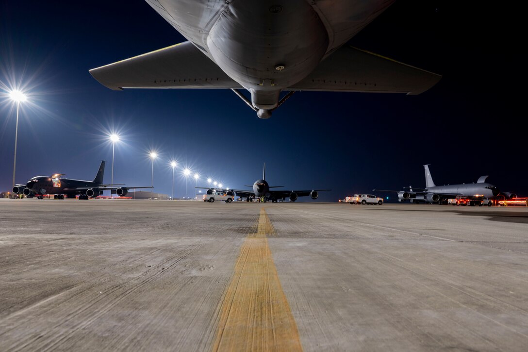 Military aircraft sit on a runway at night.