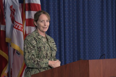 Woman stands in front of flag behind a podium