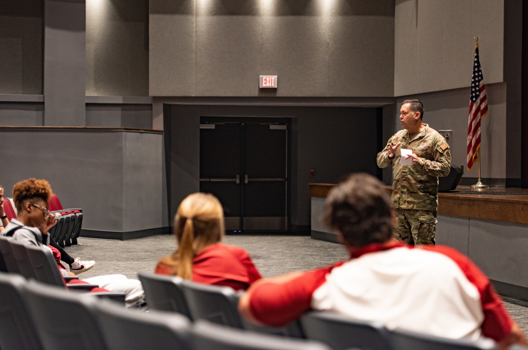 An Airmen stands in front of a crowd of student athletes in an auditorium