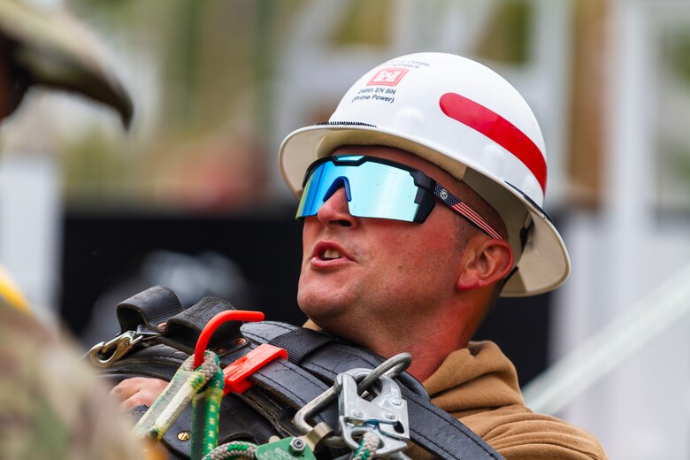 A man in a white hardhat with reflective sunglasses looks up.