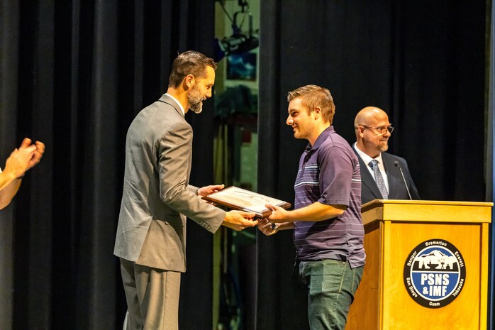 Shop 26 Superintendent Steve Dibert congratulates graduate Trevor DeClerk, welder, Shop 26, Welders, Sept. 29, 2023, during the annual Puget Sound Naval Shipyard & Intermediate Maintenance Facility Apprentice Program graduation ceremony Sept. 29, 2023, at the Bremerton High School Performing Arts Center, in Bremerton, Washington. (U.S. Navy photo by Jeb Fach)