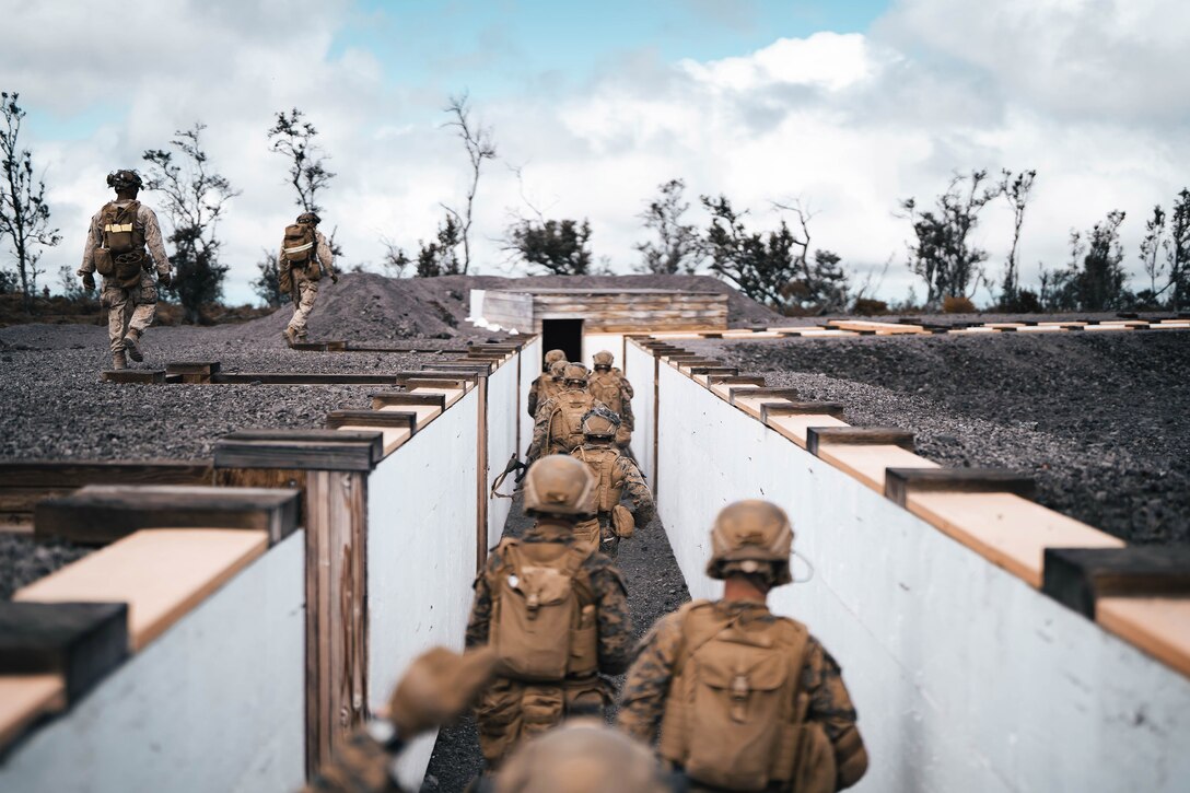 A line of Marines walk in a trench toward a door.