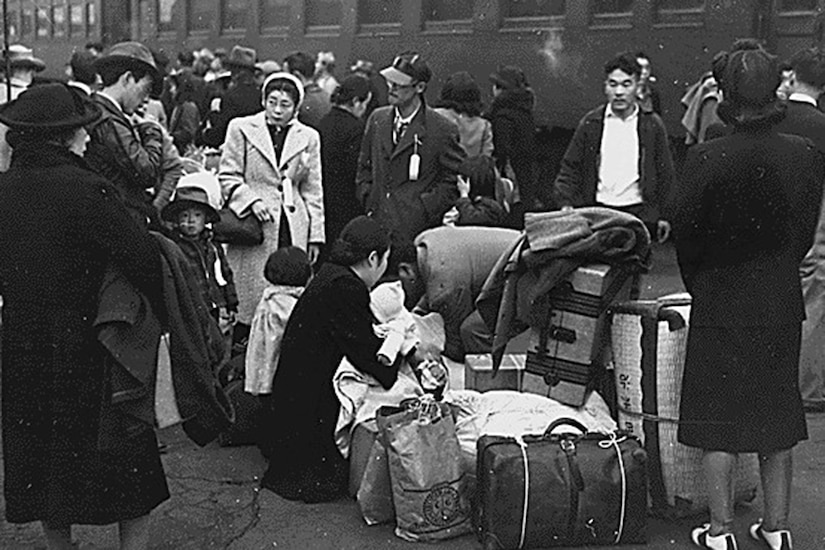 People with several suitcases and bags wait by a train.