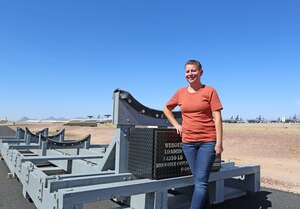 Gina Hoffman, the supervisory transportation specialist for the 309th Aerospace Maintenance and Regeneration Group (AMARG) in Tucson, Arizona, poses with an F-16 shipping fixture, Oct. 16, 2023. (U.S. Air Force photo by Rob Ranier)