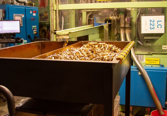 Brass ammunition casings are produced and coming out of a chute in a warehouse.