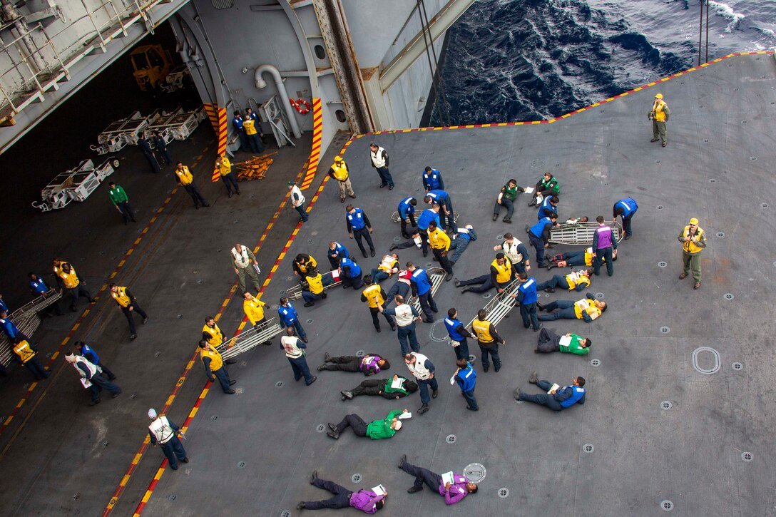Sailors lie on the deck of a ship as others stand near them.