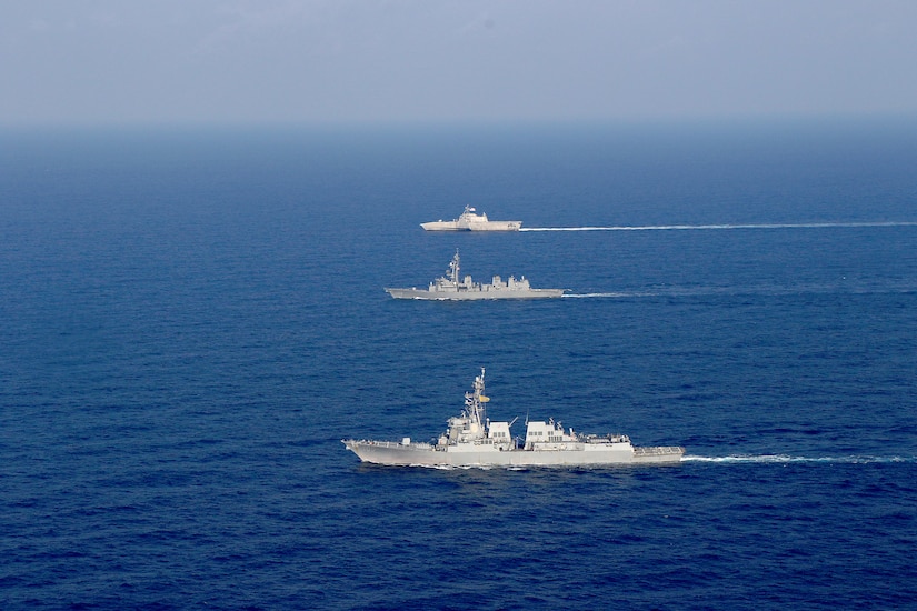 Three military ships steam next to each other.