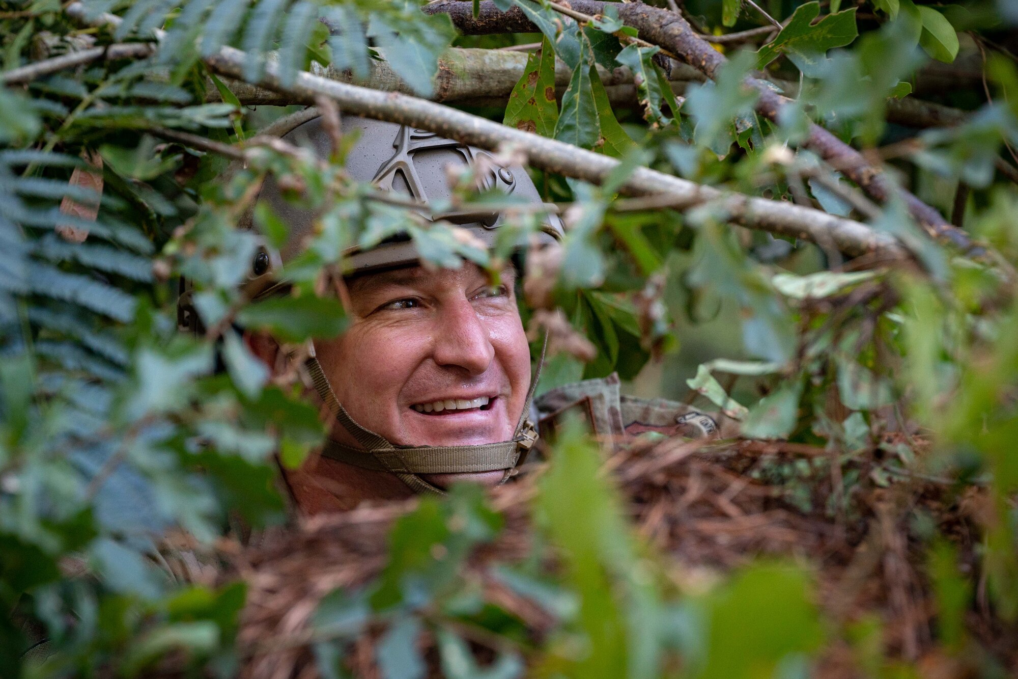 An Airman looks through foliage as he constructs a defensive fighting position.