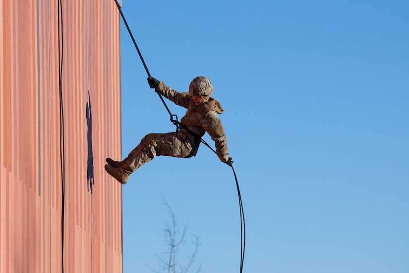A soldier rappels down a wall during training.