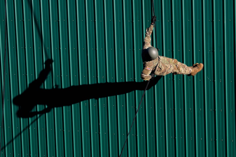 A soldier rappels down a wall. The soldier's shadow can be seen to the left.