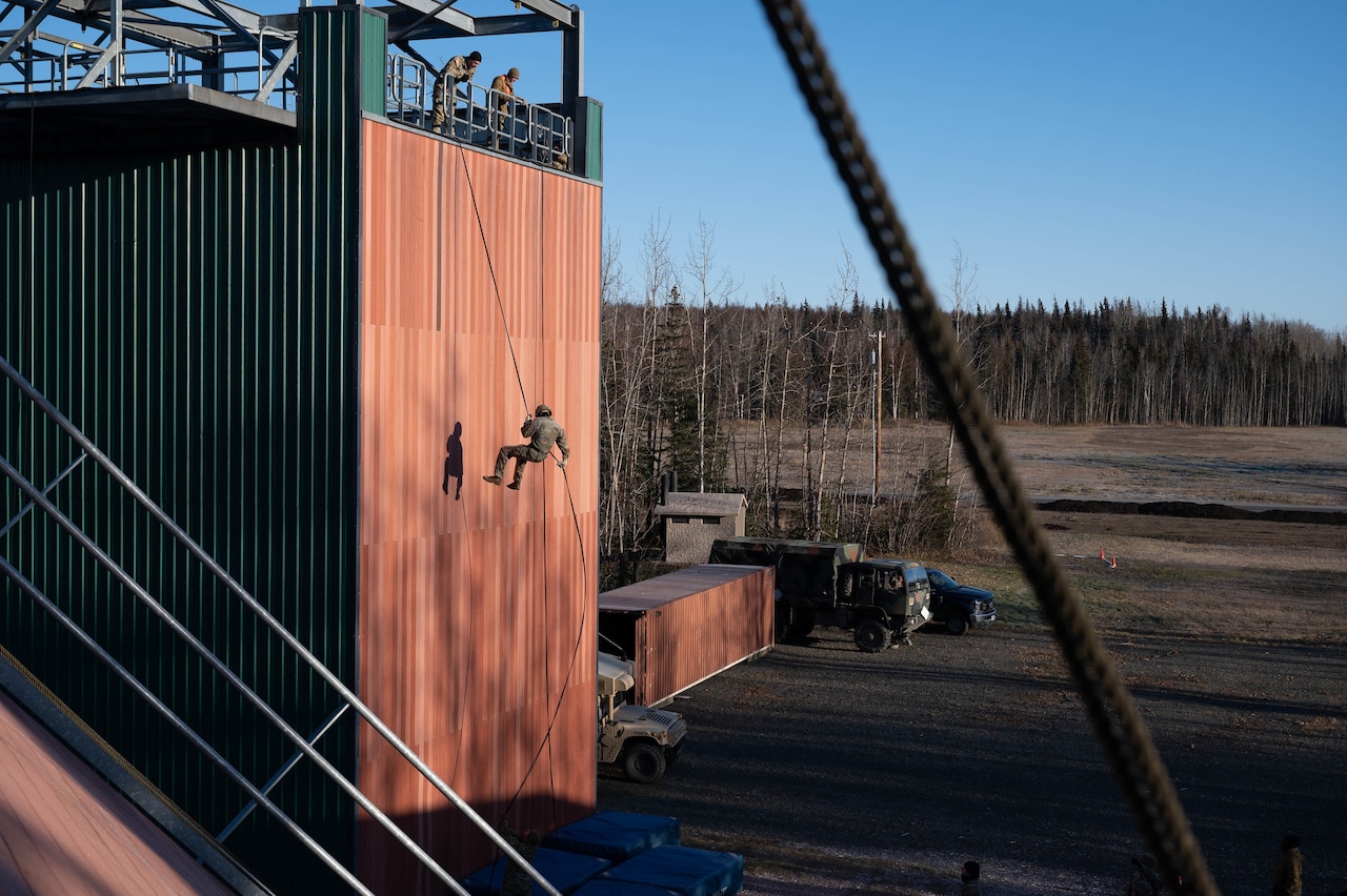 A uniformed service member participates in rappel training down a wall.