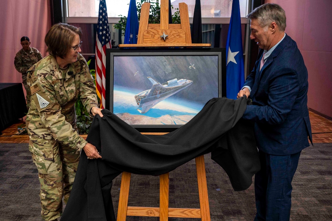 An airman and another person remove a cloth from a painting on an easel.