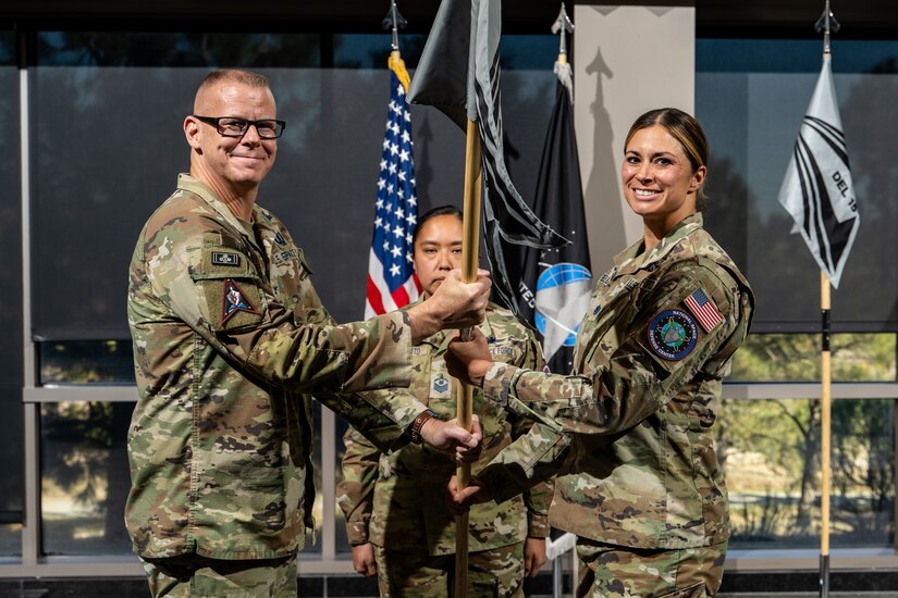 Three people stand on a stage with two holding a flag.