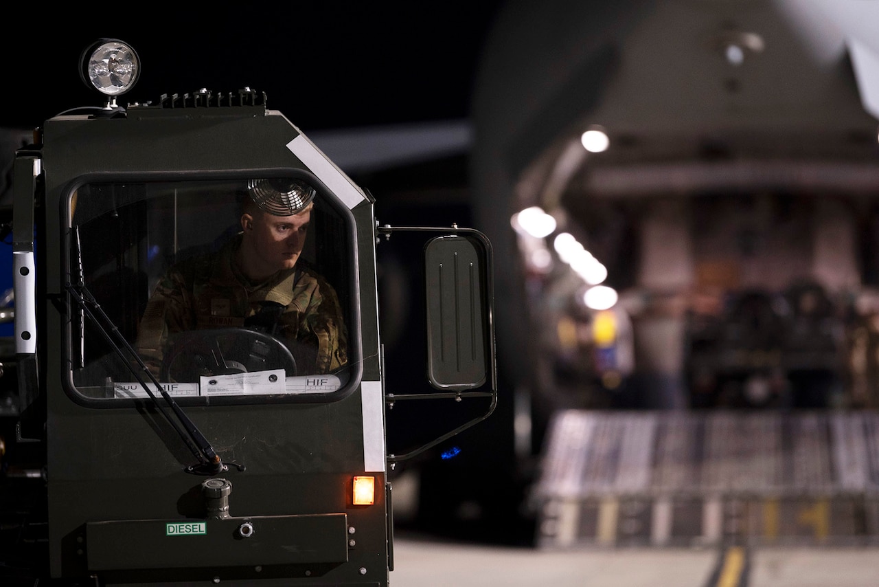 A man in uniform operates a military equipment loader.