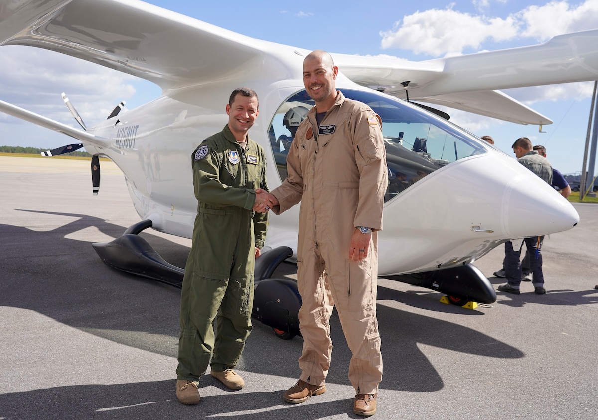 Col. Elliott Leigh, AFWERX director and chief commercialization officer for the Department of the Air Force, shakes the hand of Kyle Clark, founder and CEO of BETA Technologies, to celebrate the delivery of BETA's ALIA electric aircraft for testing at Duke Field, Florida, Oct. 26, 2023.
