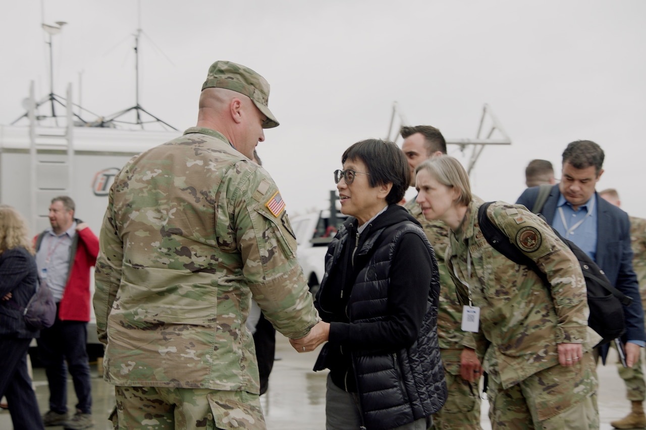 A uniformed service member shakes hands with a person in civilian clothing as others stand around them.