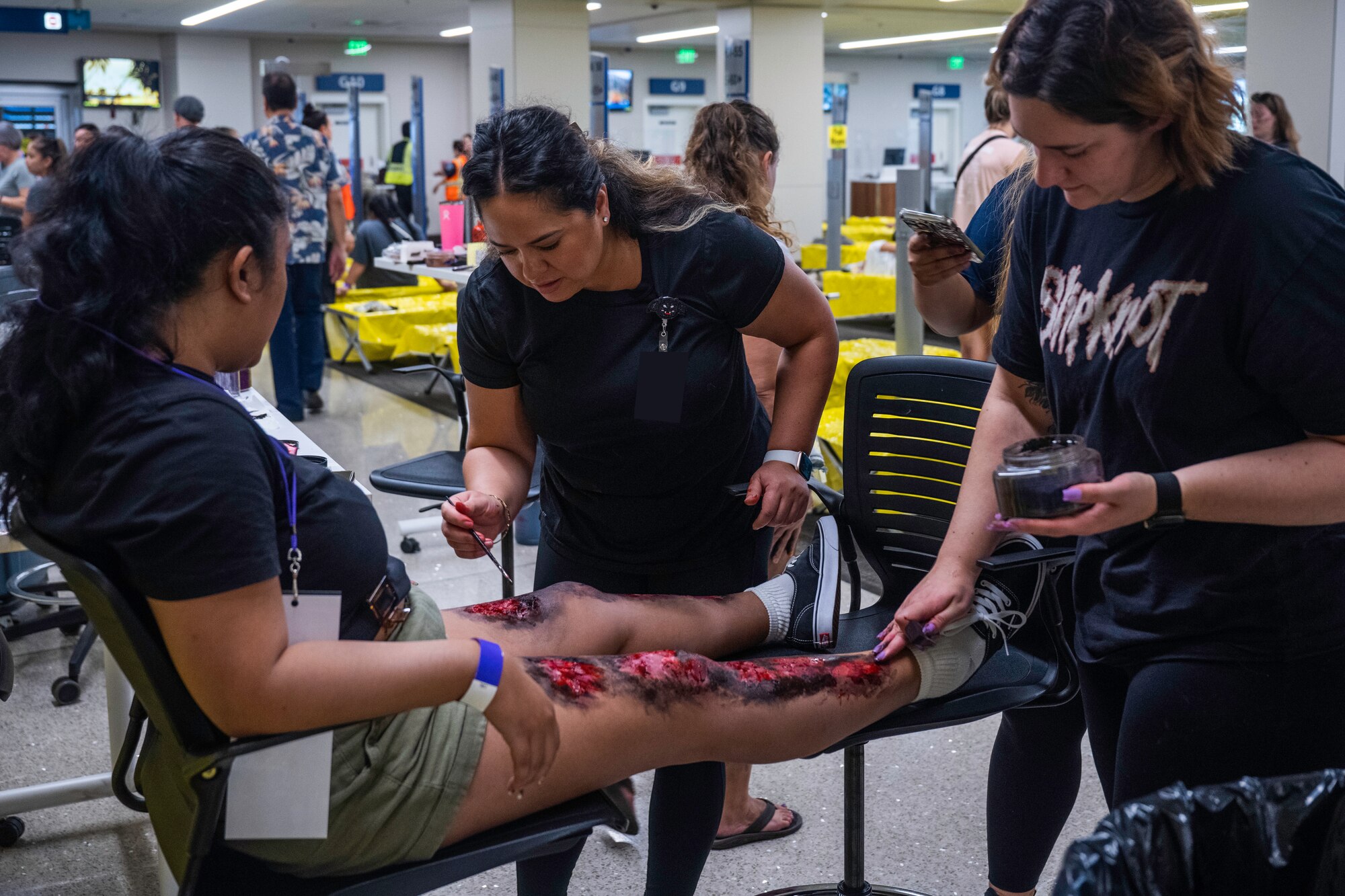 Staff Sgt. Neiliza Trinta-Santos, 15th Medical Readiness physical evaluation board liaison, and Senior Airman Sydni Breitenbach, Operational Medical Readiness Squadron bioenvironmental engineering journeyman, apply moulage makeup to a simulated patient as part of the triennial airport disaster exercise at Daniel K. Inouye International Airport, Oct. 20, 2023. Participating members included Hickam Airmen, City and County of Honolulu Fire Departments, Emergency Medical Services, American Medical Response, Federal Fire Department, U.S. Coast Guard, Federal Aviation Administration, State Department of Public Safety and nursing students from universities across the island. (U.S. Air Force photo by Senior Airman Makensie Cooper)