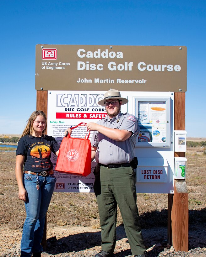 HASTY, Colo., -- Serenity Rouille placed first in the disc golf tournament, Oct. 21, 2023. The tournament was one of several events organized by USACE John Martin staff in celebration of the 75th anniversary of John Martin Dam and Reservoir. Here, John Martin Park Ranger Trevor Schuller presents Rouille with a bag of goodies, including a special 75th Anniversary commemorative disc, in recognition of her win.