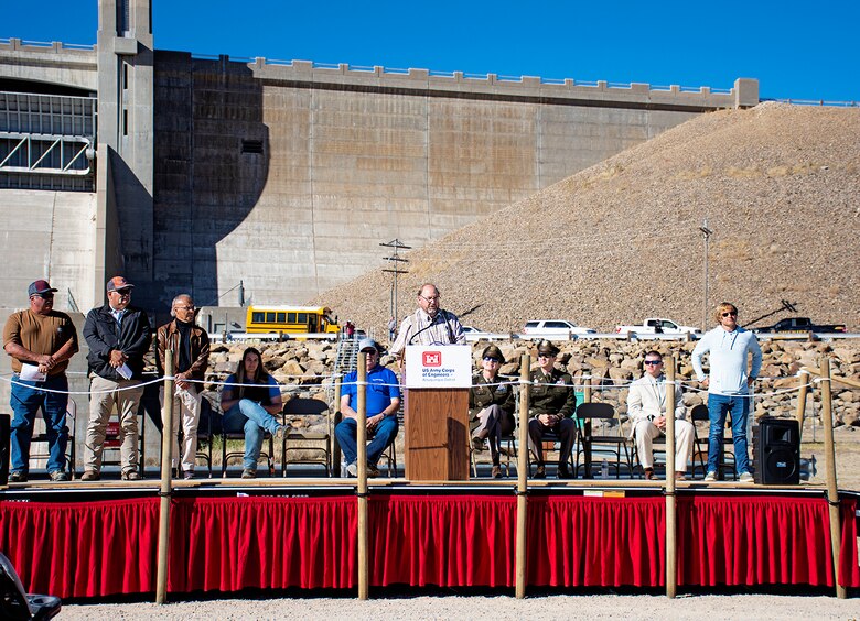 HASTY, Colo., Kevin Salter, Assistant Operations Secretary, Arkansas River Compact Administration, at podium, recognizes current and past state representatives of the ARCA present during his speech at the 75th anniversary celebration of John Martin Dam, Oct. 21, 2023. Standing, l-r: Lane Malone, Colorado representative; Scott Brazil, Colorado representative and vice chair; James Rizzuto, federal representative and chairman; and Zachary Gale, Kansas representative. Rachel Zancanella, ARCA operations secretary and division engineer with the Colorado Division of Water Resources, sits 4th from left. Zancanella was also recognized for her work with the ARCA by Salter in his speech.