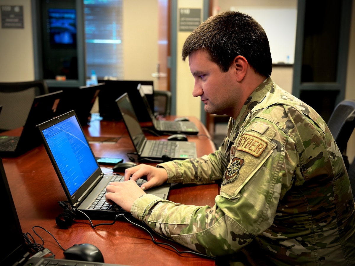 U.S. Air Force Staff Sgt. Tyler Evans sits in a room full of laptop computers and types on a computer in front of him.