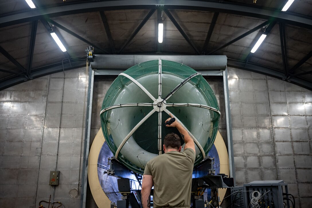 An airman stands and tests a jet engine.