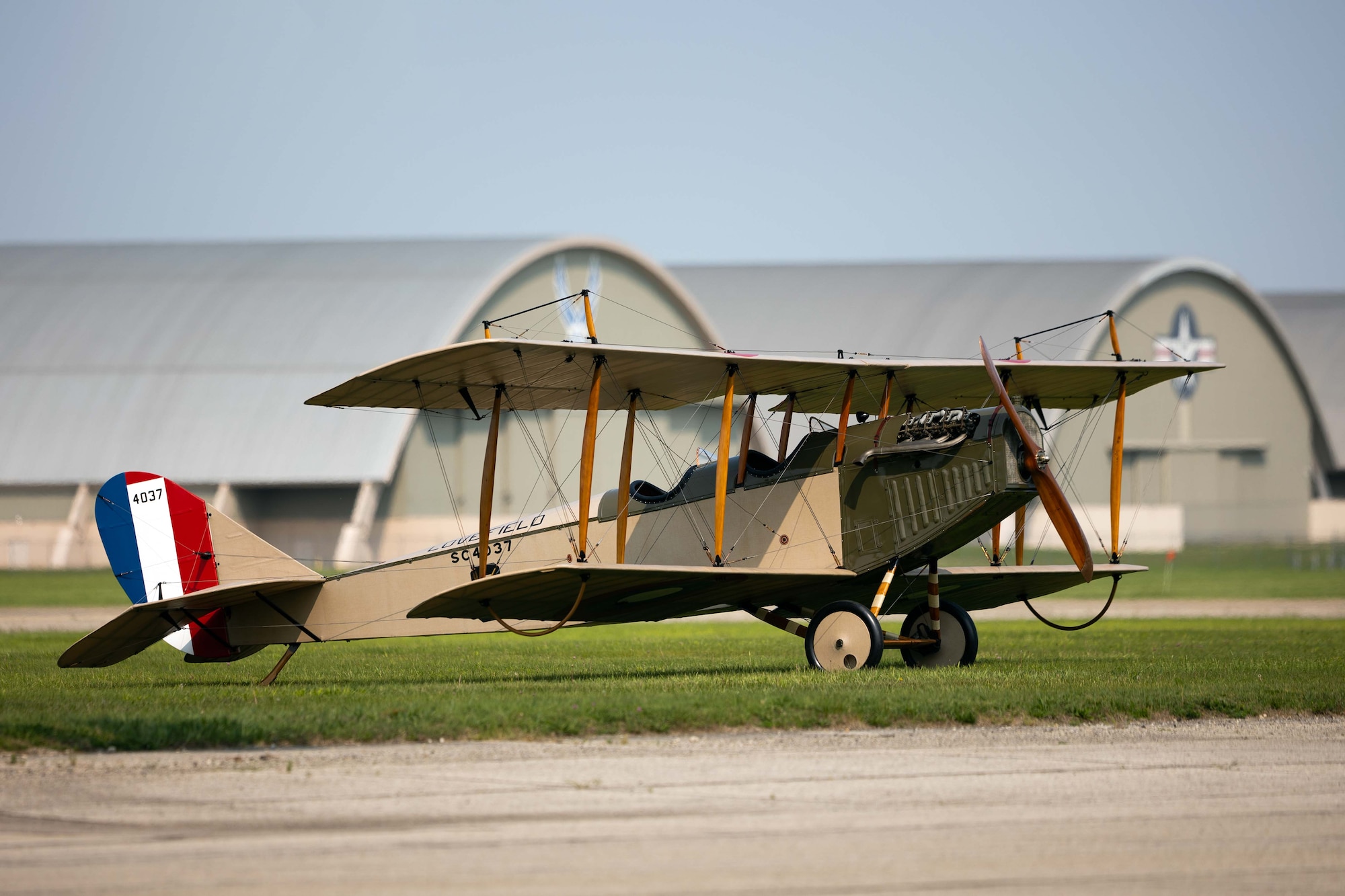 the Jenny sits in the grass with the museum complex in the distant background. the Jenny is visible from the side, featuring its tan color and the bright red, wihite and blue vertical stripes on the tail.