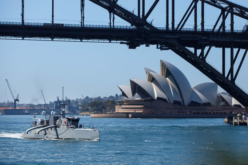 A military vessel steams under a bridge.