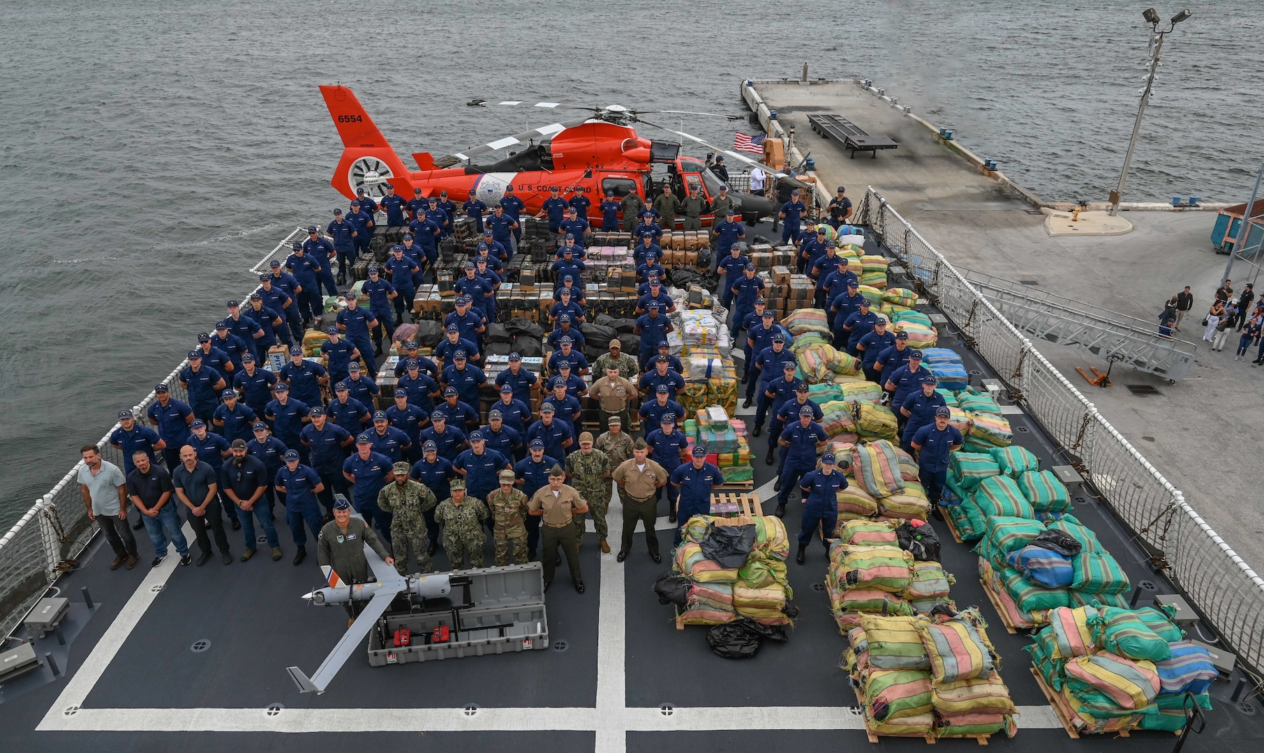 The crew of the Coast Guard Cutter James pose with more than $445 million in illegal drugs seized by Coast Guard and partner agencies in Port Everglades, Florida, Oct 26, 2023. The offload is a result of suspected drug smuggling interdictions in the Caribbean and Eastern Pacific Ocean. (U.S. Coast Guard photo by Petty Officer 3rd Class Eric Rodriguez.)