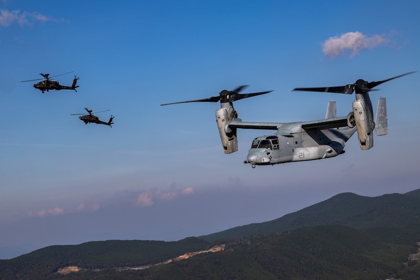 An aircraft flies near two helicopters.