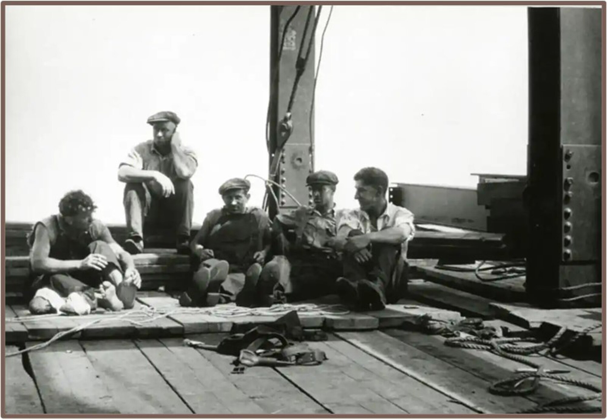 Black and white photo of five men sitting on the floor of a construction site