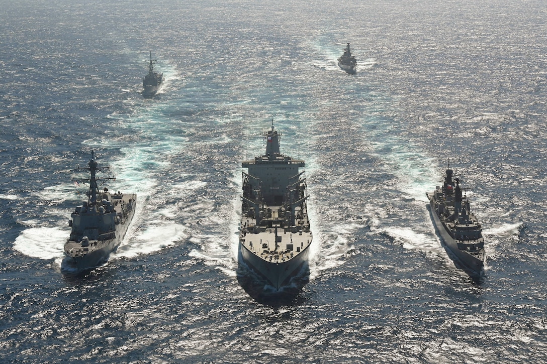 Three ships sail next to each other as two ships sailing in formation follow.