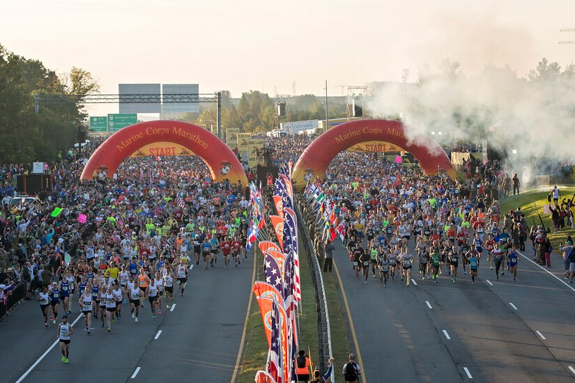 Smoke wafts above hundreds of people running on two highways under arched Marine Corps Marathon signage.