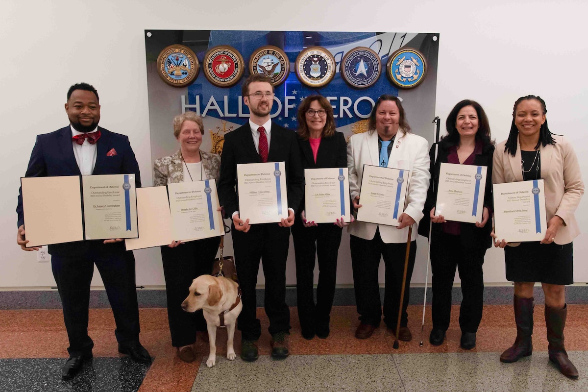 A group of people in civilian attire pose for a photo while holding award certificates.