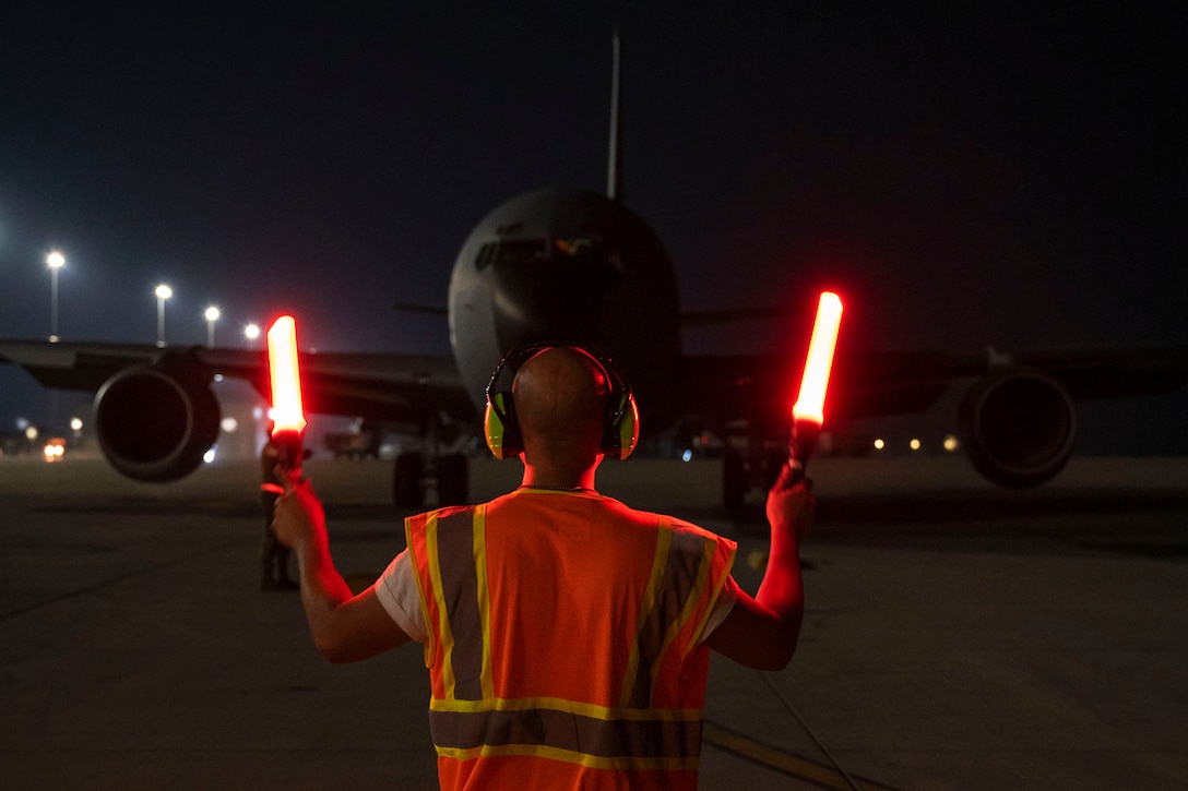 An airman holding light flares gives landing directions to an Air Force KC-135 at night.