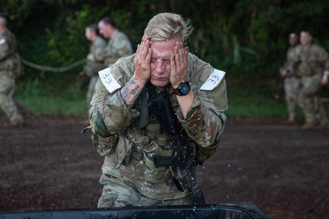 A soldier washes his face as other soldiers run behind him.