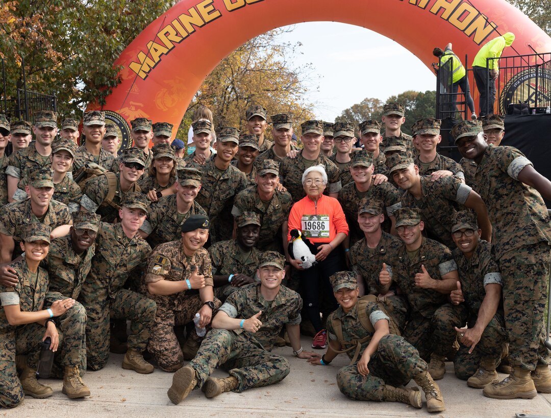 U.S. Marines and a member of the Mongolian military celebrate with last runner in the 48th Marine Corps Marathon and Penguin Award winner, Soon Kim, in Arlington, Virginia, Oct. 29, 2023. The Penguin Award is presented in honor of the life and service of Public Affairs Officer and marathon runner Maj. Megan McClung who was killed in action in Iraq in December 2006. (U.S. Marine Corps Photo by Sgt. Bryce Hodges)