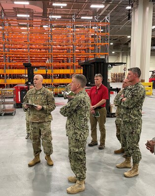 Five men stand in warehouse looking at an unseen object.