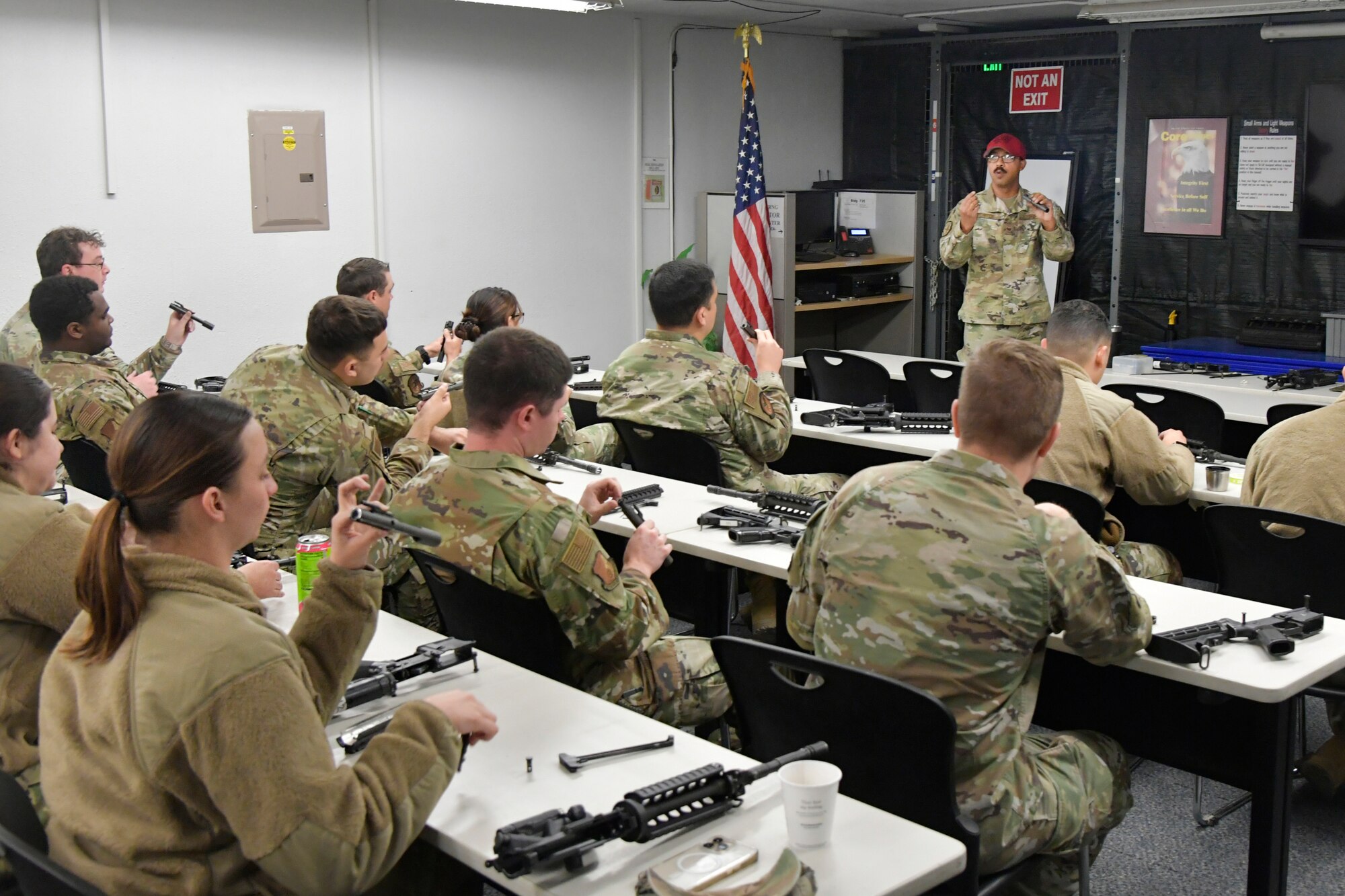 An instructor leads a class of Airmen who have weapons parts on the desk.