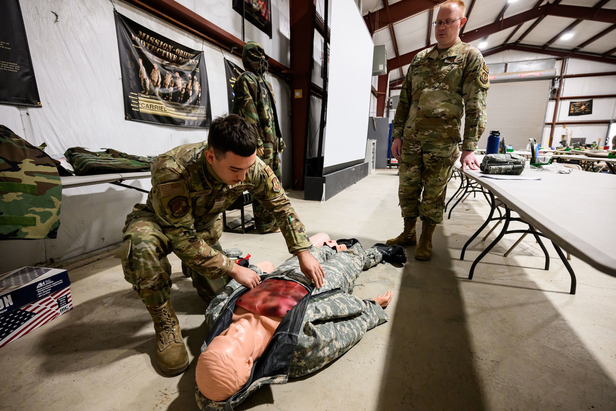 An Airman works on a lifelike training aide with an instructor standing behind