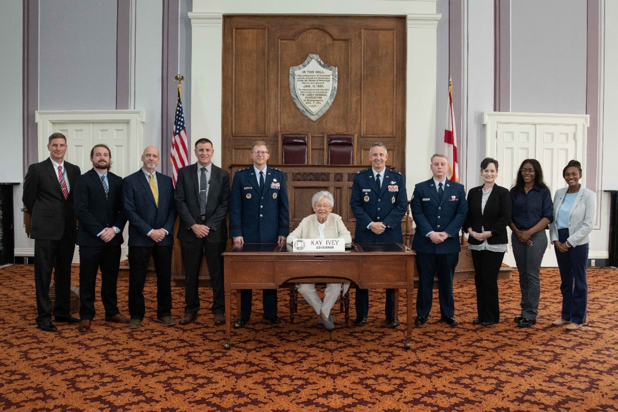 Air Force Culture and Language Center personnel, along with Maj. Gen. Parker Wright and Col. Robert Rowell, watch as Alabama Governor Kay Ivey signs a proclamation on Oct. 2, 2023, declaring the month of November as Language, Regional Expertise, and Culture Month in honor of the Air University LREC Symposium at Maxwell Air Force Base, Ala. L-R: Scott Alford, Riley Hunt, Greg Day, Walter Ward, Maj. Gen. Parker Wright, Gov. Ivey, Col. Robert Rowell, Senior Airman Corbin Miller, Lori Quiller, TaeAjah Cannon-Barnes, and Mikala McCurry.
