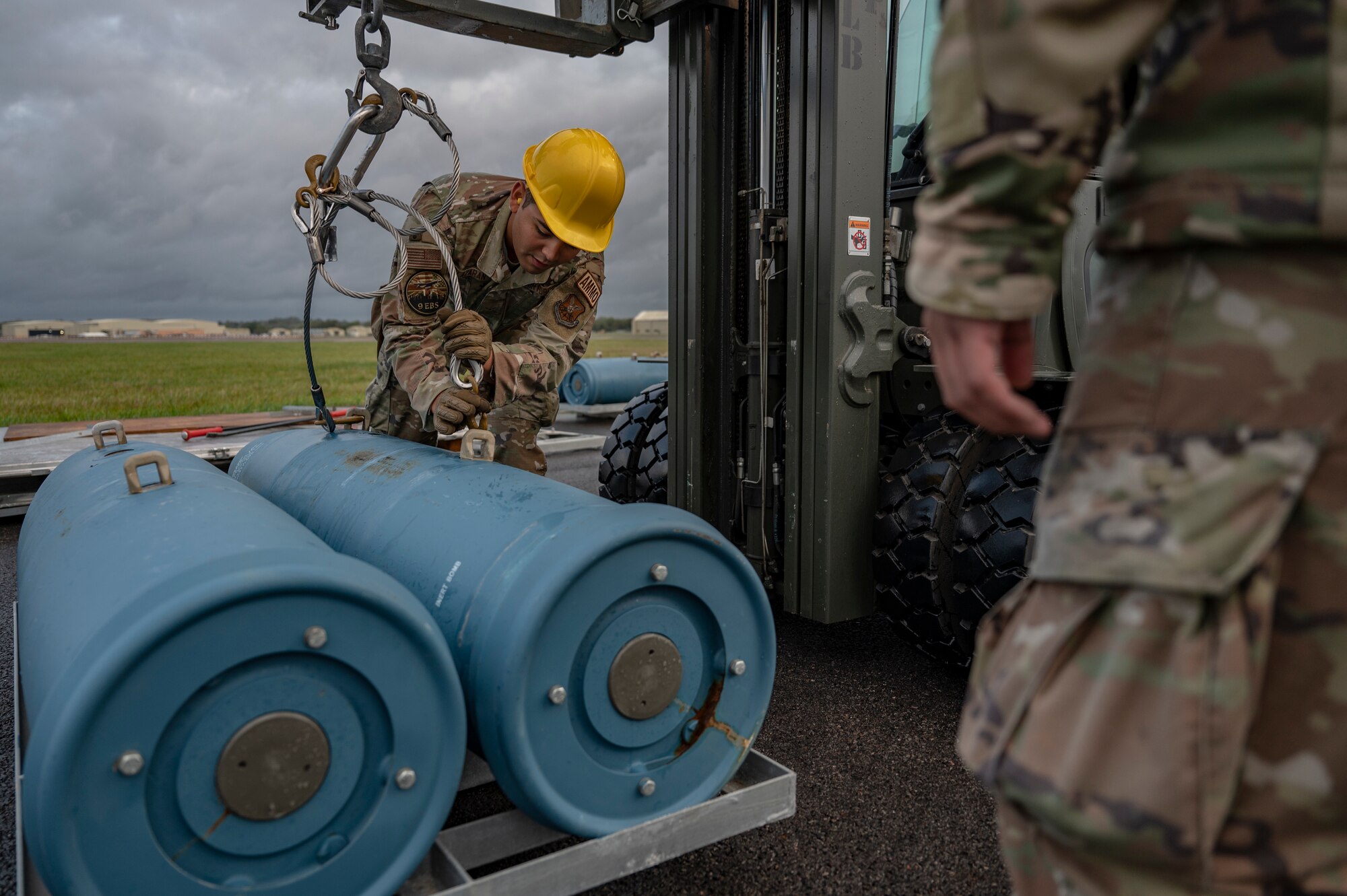 Airman 1st Class Hector Olazaran, 9th Expeditionary Bomb Squadron line delivery crew chief, prepares an inert bomb to be lifted by a forklift during an inert ammo bomb building event at RAF Fairford, United Kingdom, Oct. 13, 2023. U.S. Strategic Command regularly tests and evaluates the readiness of assets to ensure deterrence is strong and credible. (U.S. Air Force Photo by Senior Airman Ryan Hayman)