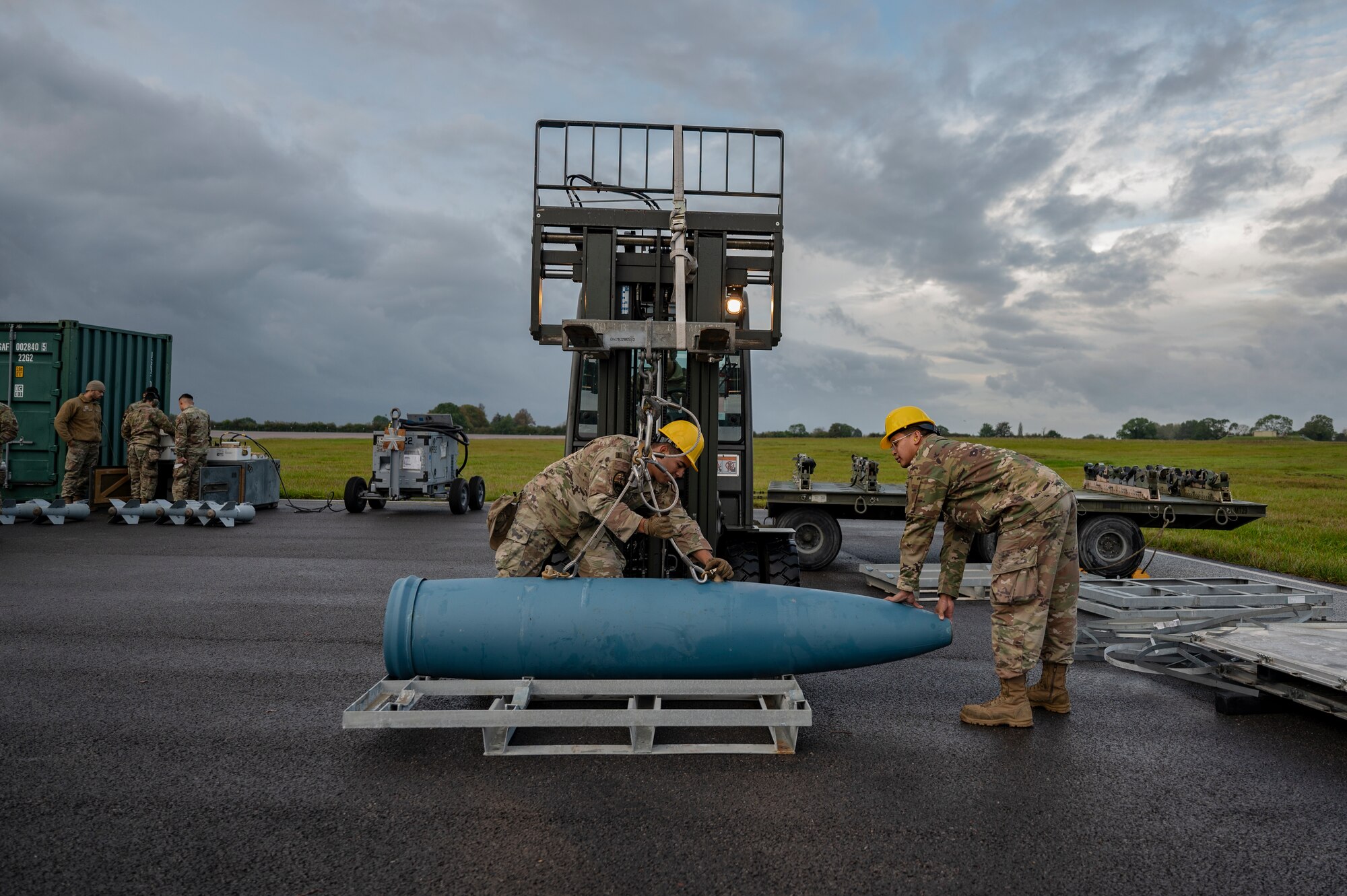 Airman 1st Class Hector Olazaran, 9th Expeditionary Bomb Squadron line delivery crew chief, and Senior Airman Isaiah Rogado, 9th EBS weapons load crew specialist,  prepares an inert bomb to be lifted by a forklift during an inert ammo bomb building event at RAF Fairford, United Kingdom, Oct. 13, 2023. Bomber Task Force missions enable crews to maintain a high state of readiness and proficiency, validating our always-ready, global strike capability. (U.S. Air Force Photo by Senior Airman Ryan Hayman)