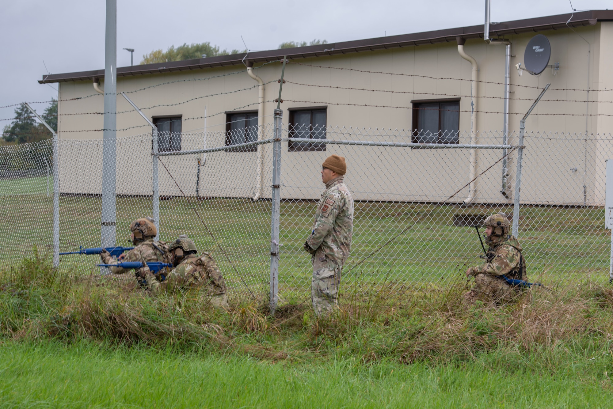 Airmen crouch alongside a fence