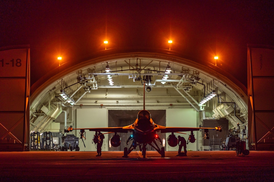 Airmen inspect a military aircraft on the tarmac at night.