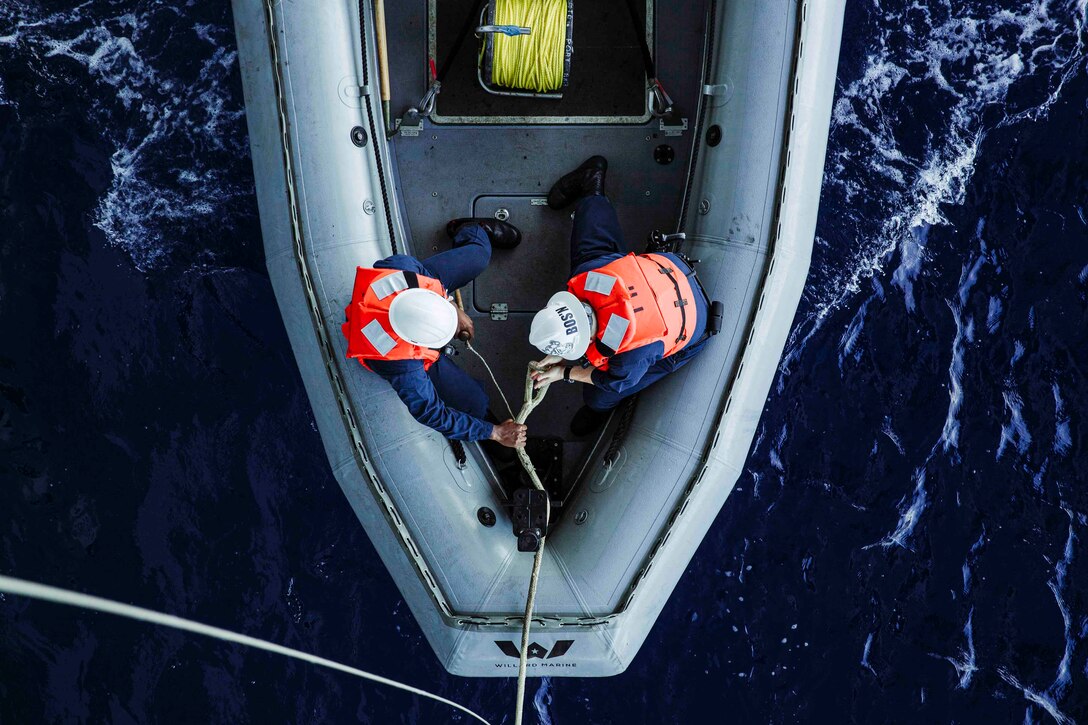 An overhead look at two sailors holding onto a line while sitting in an inflatable boat.