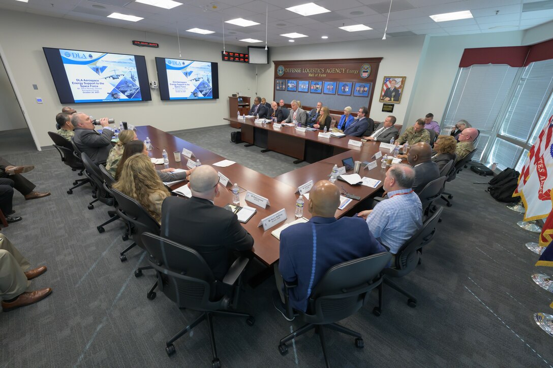 People are seated around three tables in a conference room for a meeting.