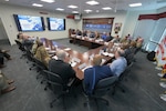 People are seated around three tables in a conference room for a meeting.