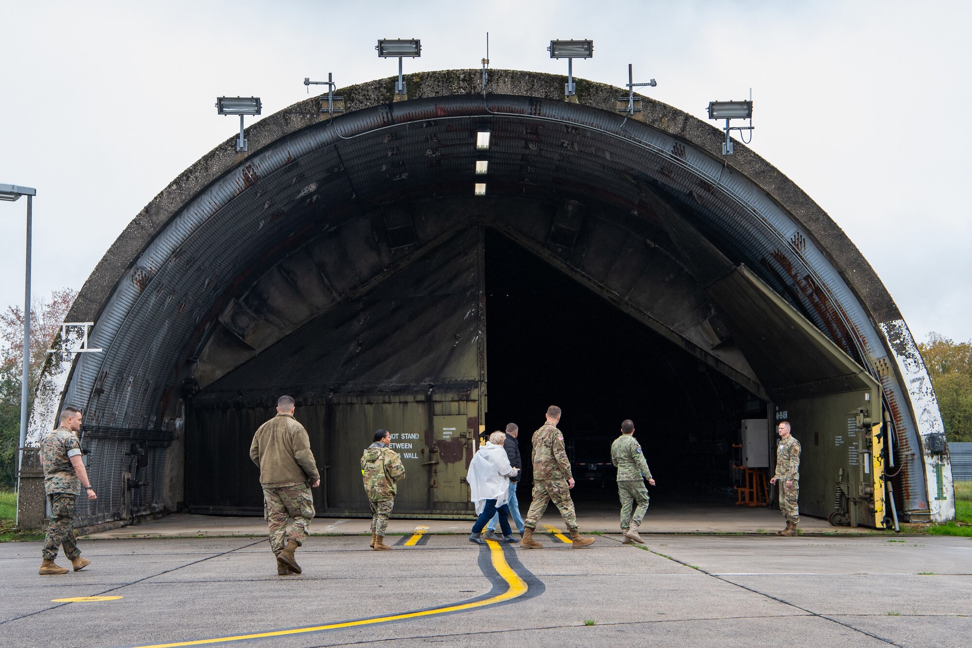 U.S. service members, Romanian service members and civilians walk towards an empty, half-open aircraft hangar.
