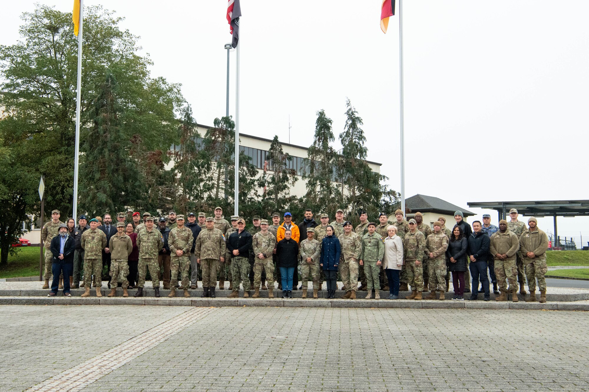 U.S. service members, Romanian service members and civilians pose for a photo in front of flag poles.